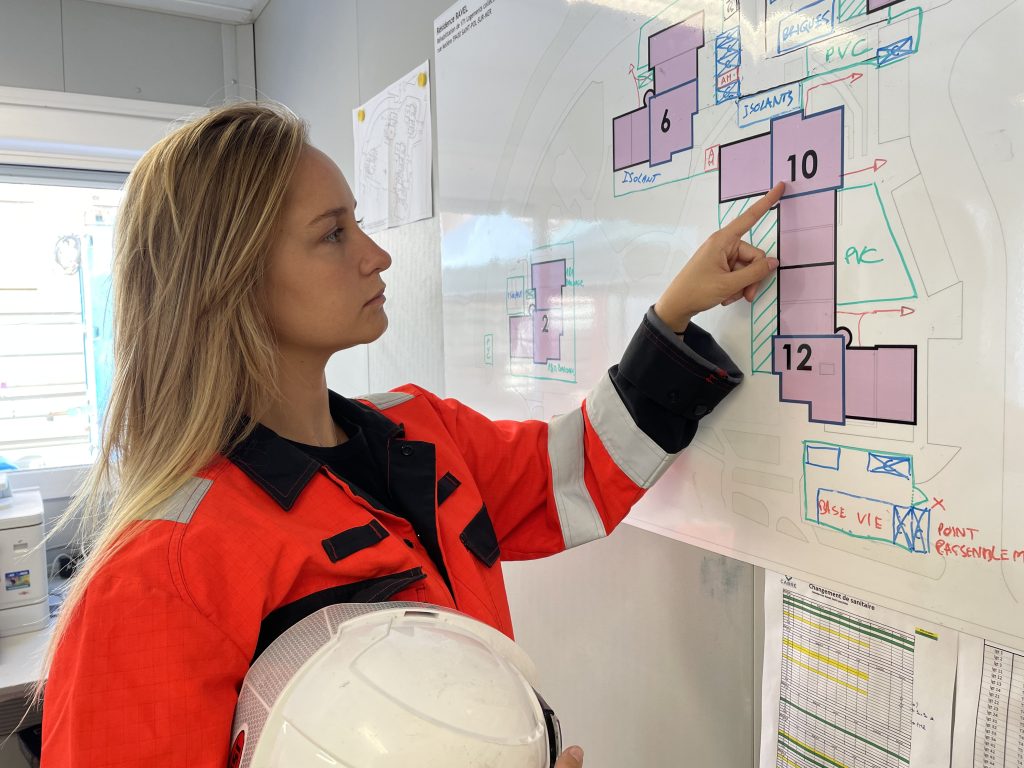 Jeune femme équipée d'un équipement de protection personnel. Elle pointe une partie précise d'un plan.